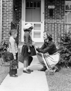 Mother outside front door, buttoning sweater of daughter going off to school with her brother. (Photo by H. Armstrong Roberts/Retrofile/Getty Images)