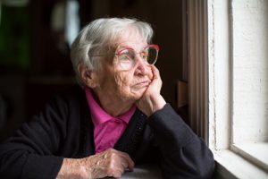 Elderly woman in glasses thoughtfully looking out the window.